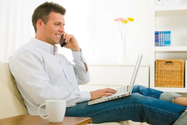 man on couch talking on phone and working on laptop