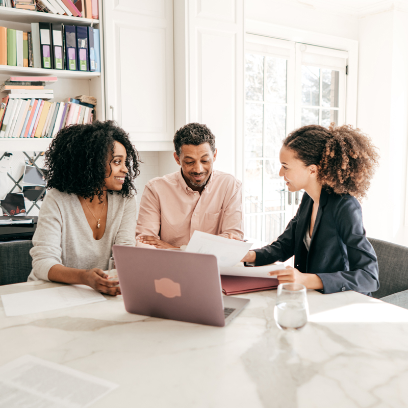 3 people sit down with paperwork and a laptop