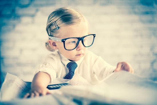 Business child with glasses sitting at blurred out messy desk