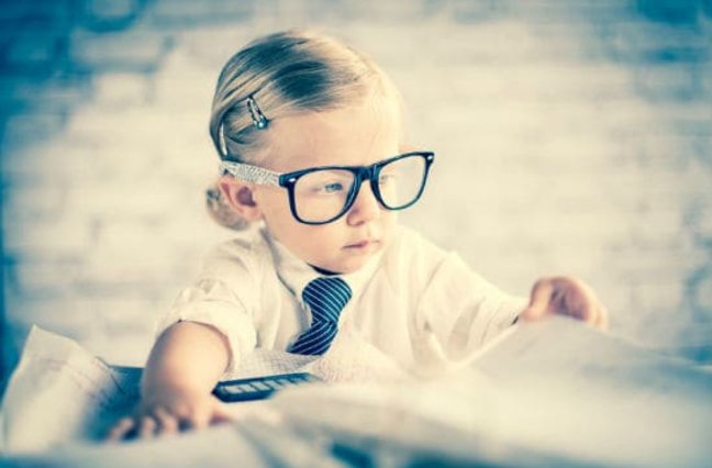 Business child with glasses sitting at blurred out messy desk