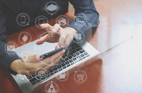 businessman in front of laptop looking at phone with omnichannel tech graphic icons