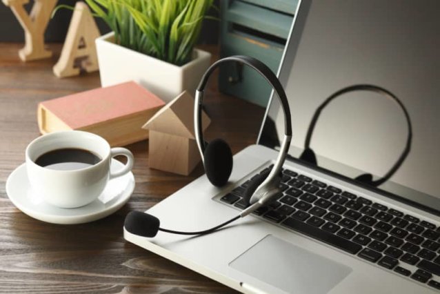 office desk with laptop, cup of coffee and headset on wooden table