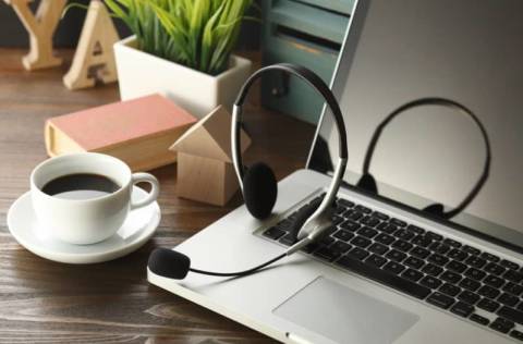 office desk with laptop, cup of coffee and headset on wooden table