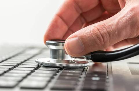Conceptual image of the hand of a man checking the health of his laptop computer using a stethoscope as he checks for malware and viruses or any electronic malfunctions.