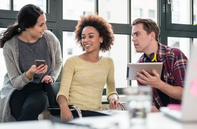 Three employees look at an iPhone and iPad.