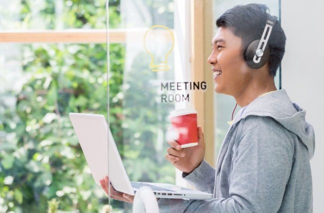 Man holds coffee while taking a phone call near a window.