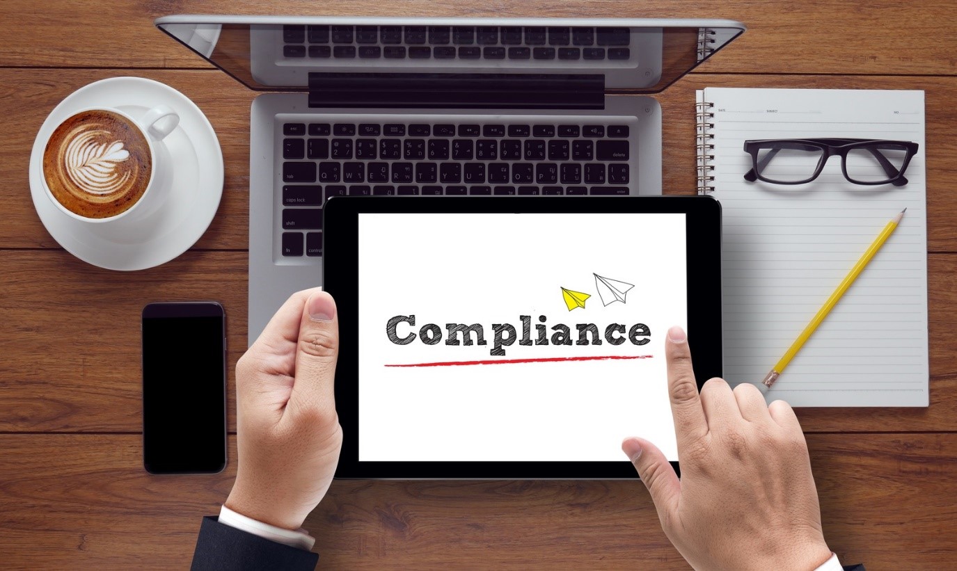 looking down at a clean desk businessman's hands holding tablet with Compliance graphic