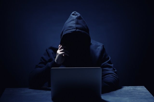 mystery person wearing hoodie in front of laptop