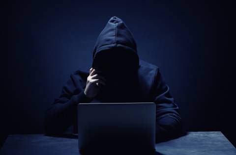 mystery person wearing hoodie in front of laptop