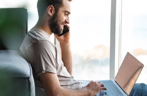 Man talks on phone while using laptop