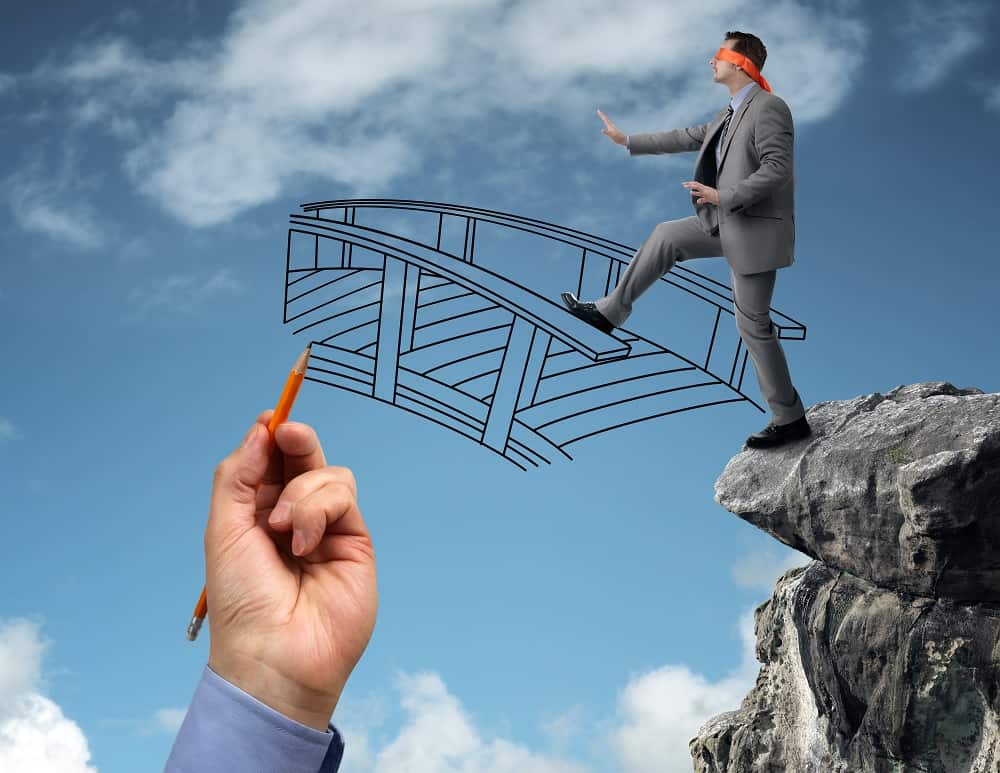 blindfolded businessman walking onto drawing of bridge