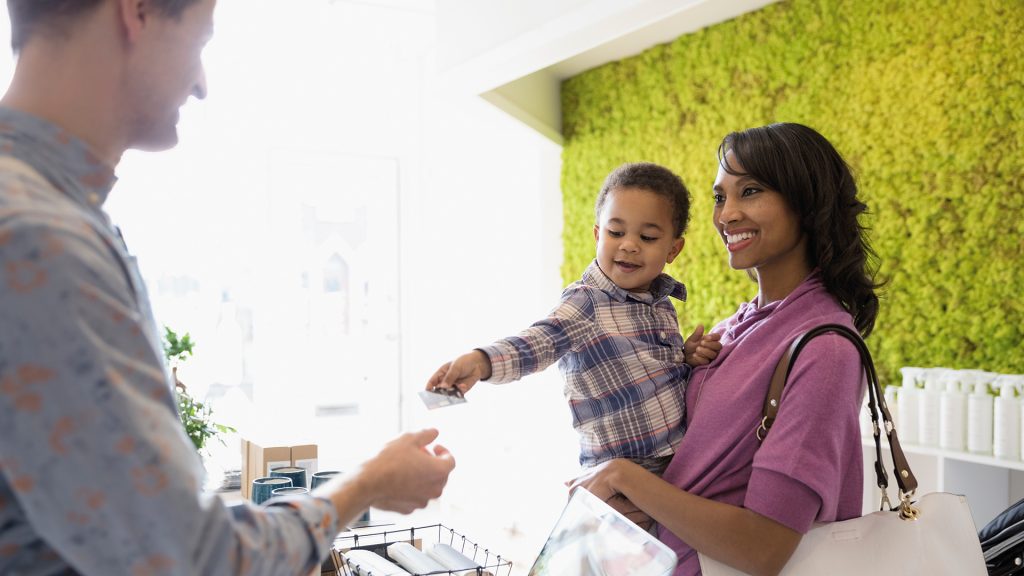 L woman holding toddler handing credit card to cashier