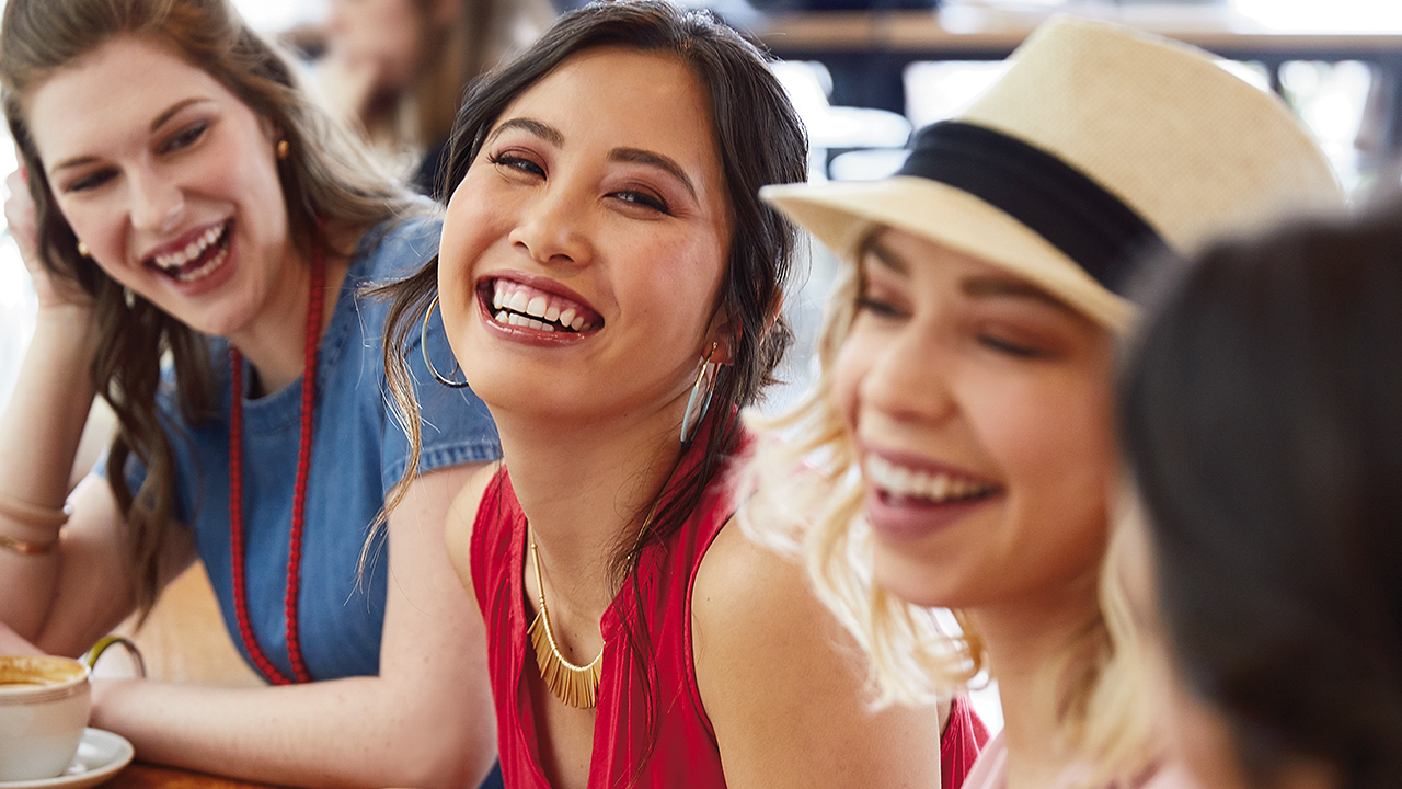 Four female friends laughing smiling at cafe