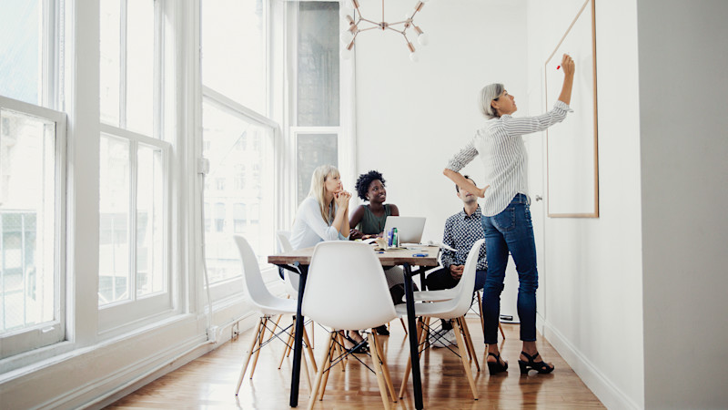 L woman at whiteboard with three coworkers