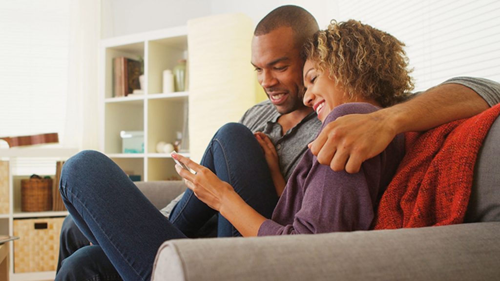 L couple cuddling on couch looking at mobile phone