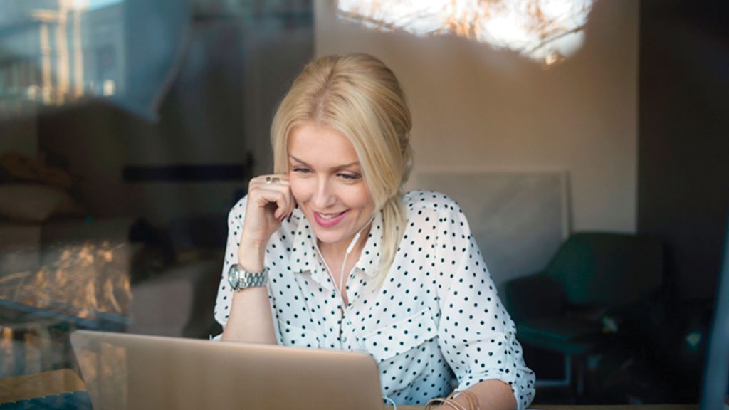 L female smiling at laptop earbuds coffee shop