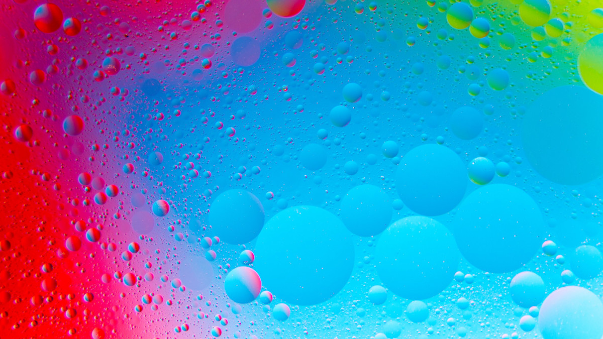Wassertropfen auf einer beschlagenen Glasscheibe in intensiv farbigem Licht von Rot über Blau bis Grün