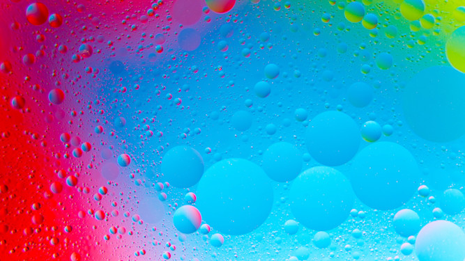 Wassertropfen auf einer beschlagenen Glasscheibe in intensiv farbigem Licht von Rot über Blau bis Grün