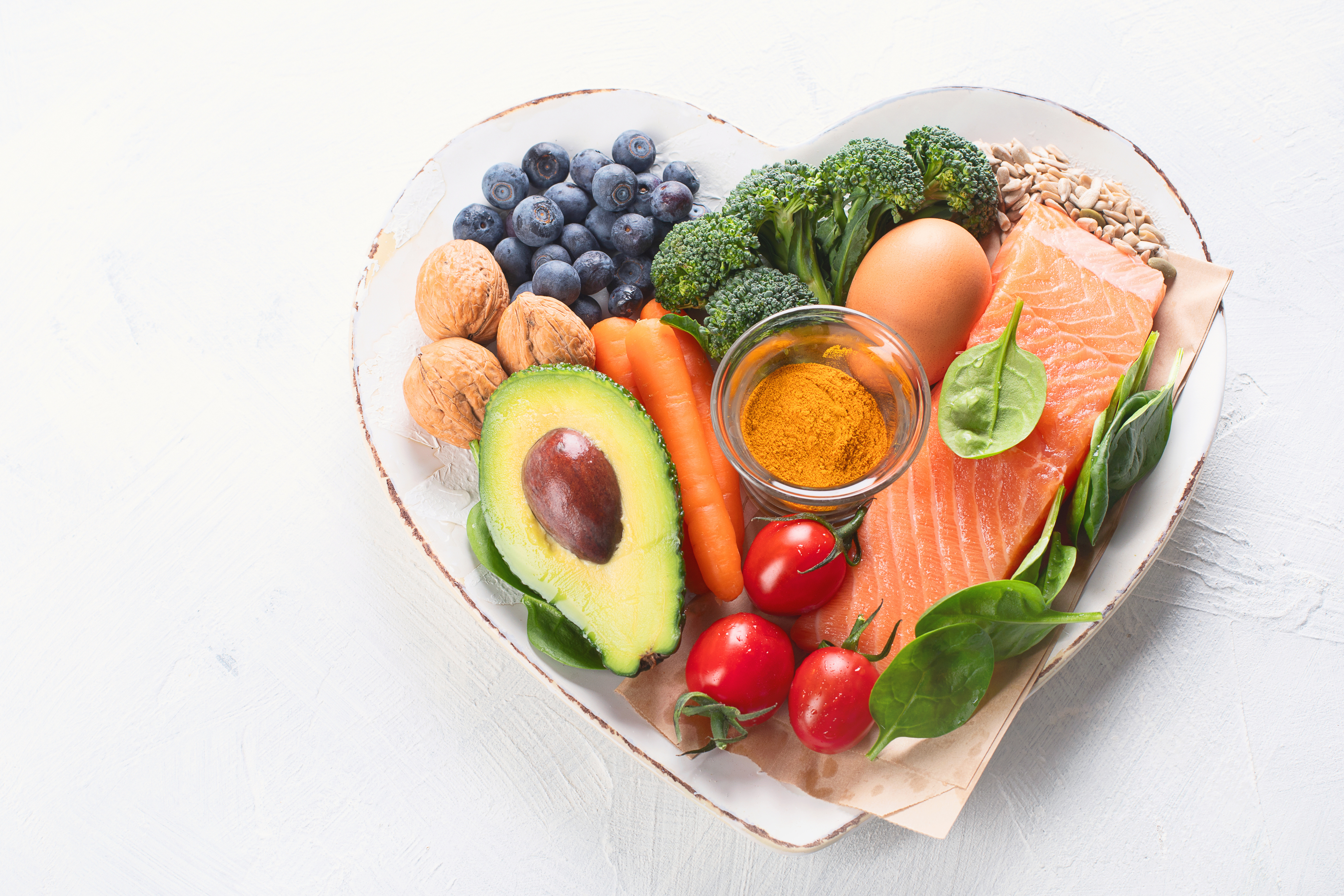 Lax, grönsaker, bär, ägg, gurkmeja på vit hjärtformad tallrik - iStock-1135886728