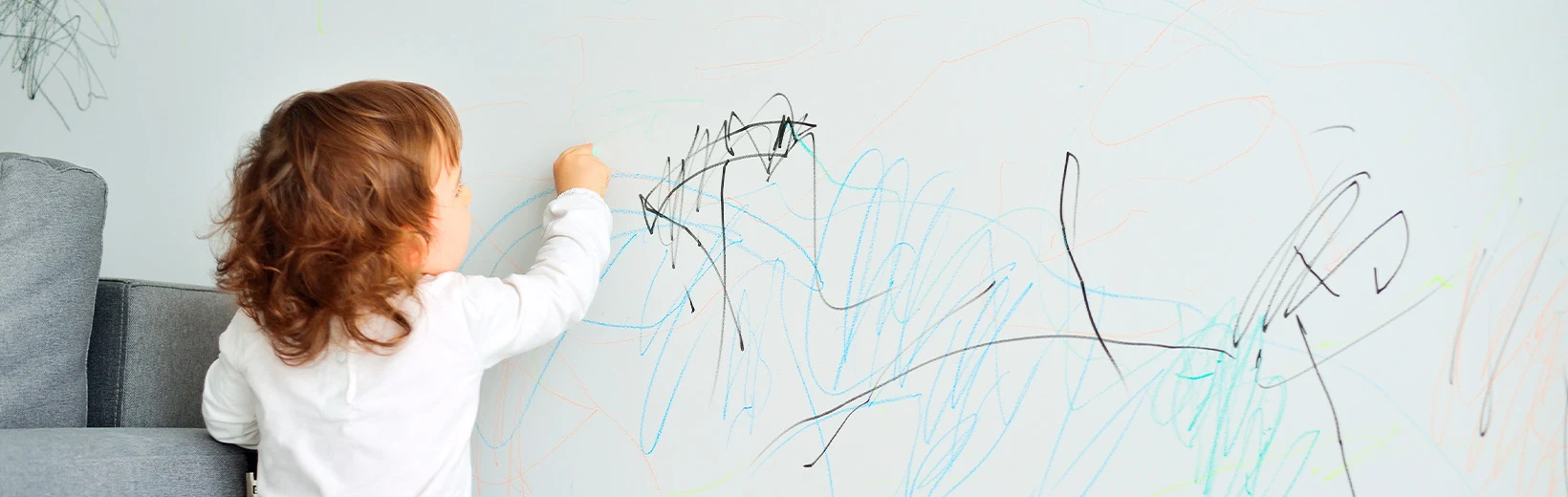 A child draws with felt-tip pens on a white wall