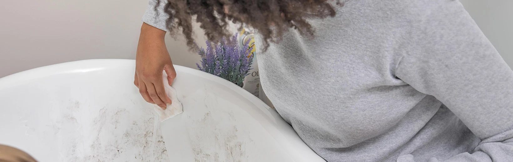 A girl with a curly hair cleaning a dirty bathtub, lavender is visible in the background