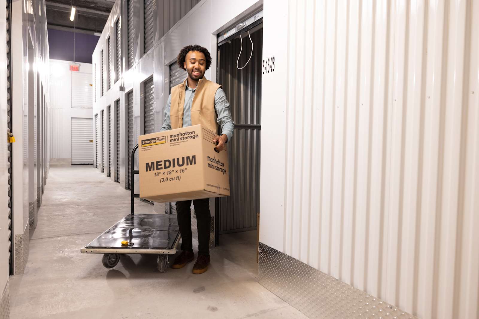 A Man is loading a Manhattan Mini Storage moving box into his self storage unit from a moving cart