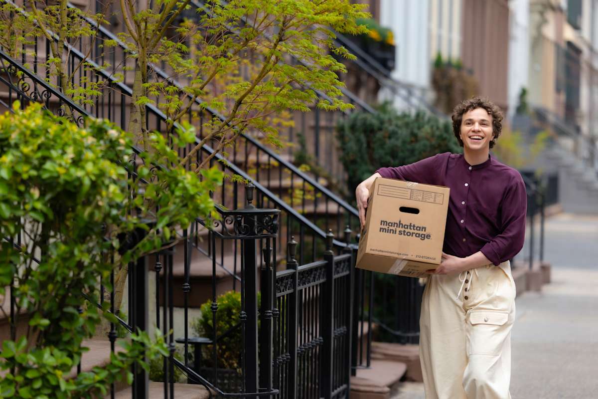 Smiling customer with a Manhattan Mini Storage moving box walking down the street