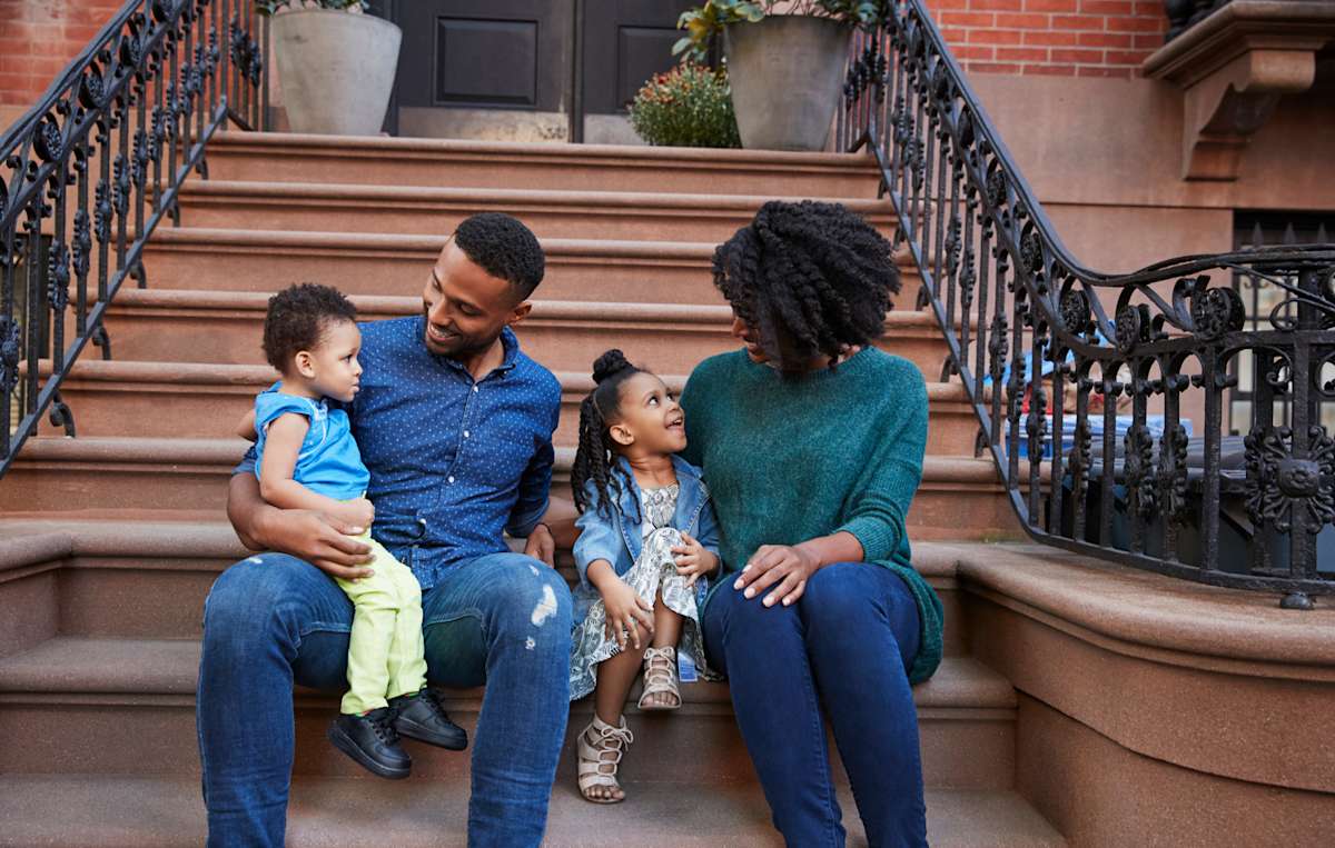 A family sits on the front steps of their brownstone