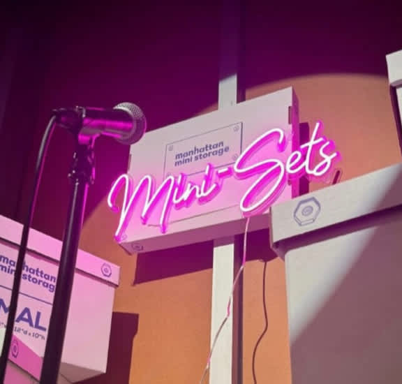 neon lights reads mini-sets in front of a Manhattan Mini Storage moving box