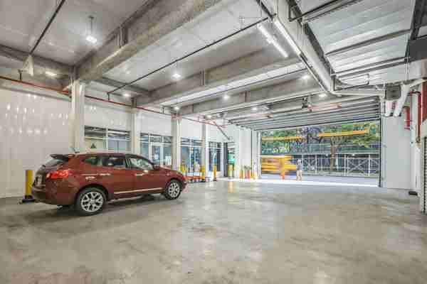 Clean, well-lit indoor loading bay with high ceilings, yellow safety bollards, a parked SUV, and rolling carts near storage unit entrances