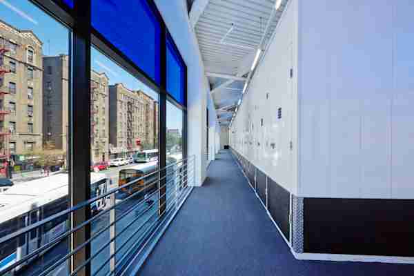 Interior hallway of a modern self-storage facility at 5030 Broadway in New York City, featuring white unit doors, blue carpet, and large windows overlooking city traffic and historic brick apartment buildings.