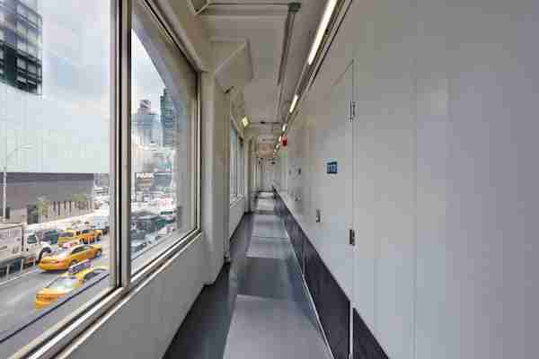 Interior hallway of Manhattan Mini Storage at 260 Spring Street, New York City, with white storage unit doors on the right, large windows on the left overlooking busy city traffic and yellow taxis, and modern urban buildings outside.