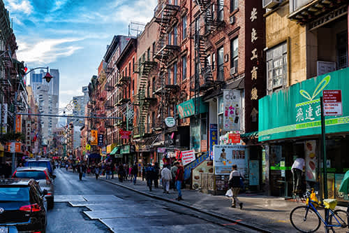 Busy Chinatown street in New York City lined with shops, restaurants, and people walking.