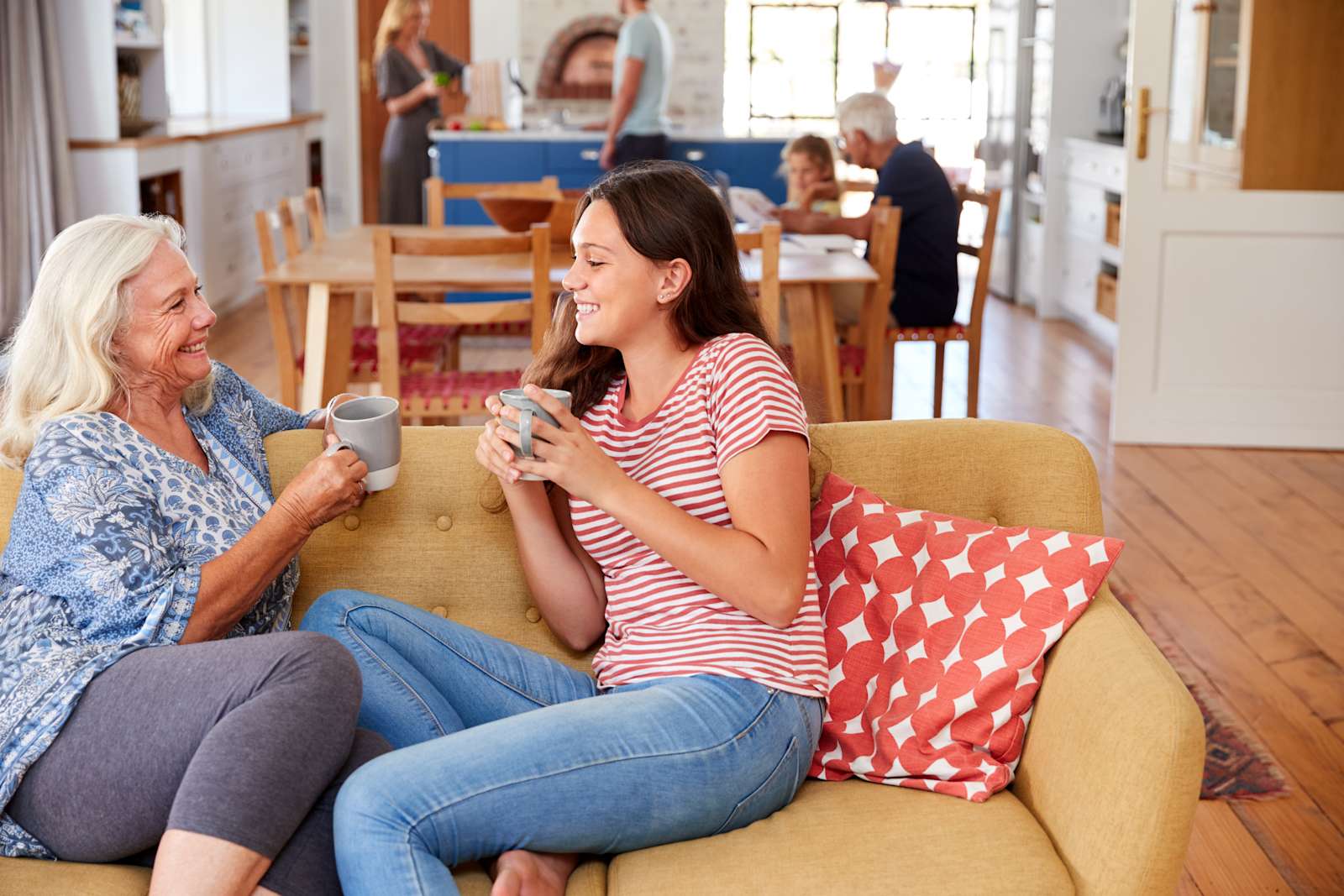 A young girl sits on the couch with her grandmother drinking coffee