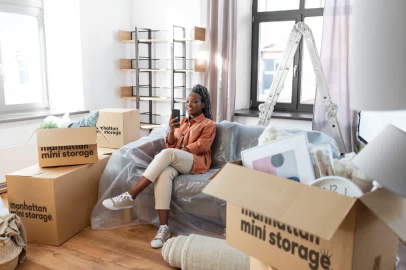 A woman sits on the couch on her phone with Manhattan Mini Storage moving boxes around her