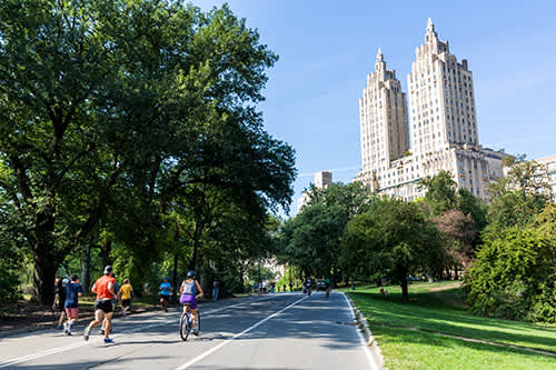 Cyclists on a path near a large building, surrounded by greenery and clear skies.