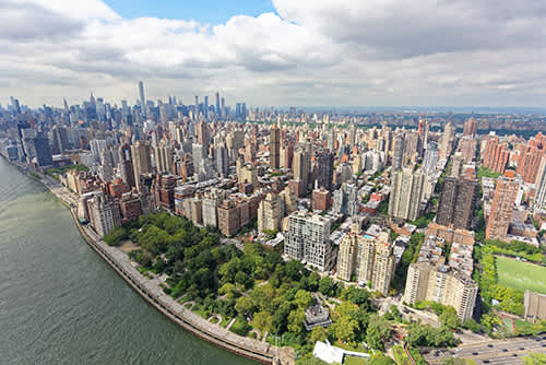 Aerial view of Manhattan's Upper East Side with park, river, and skyline in the distance.