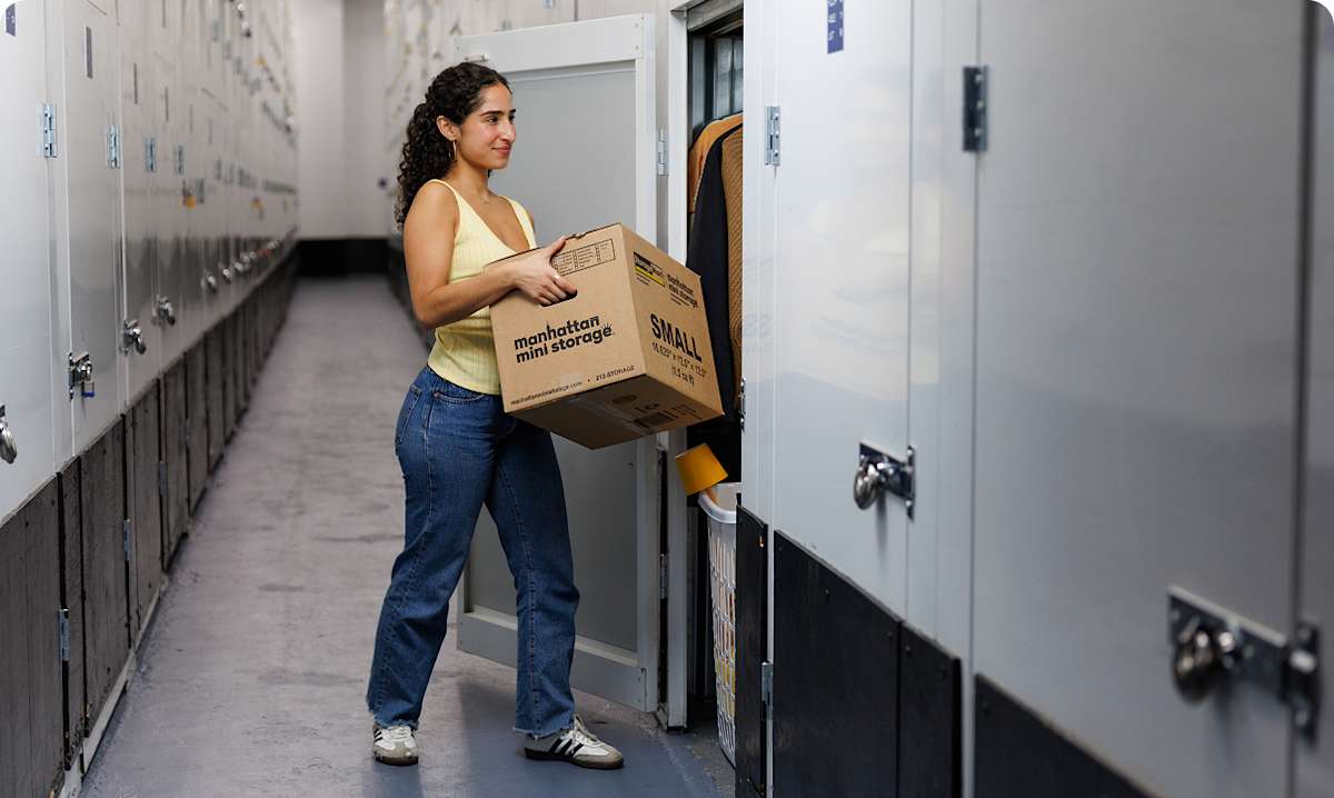 A young woman puts a Manhattan Mini Storage moving box into a storage closet
