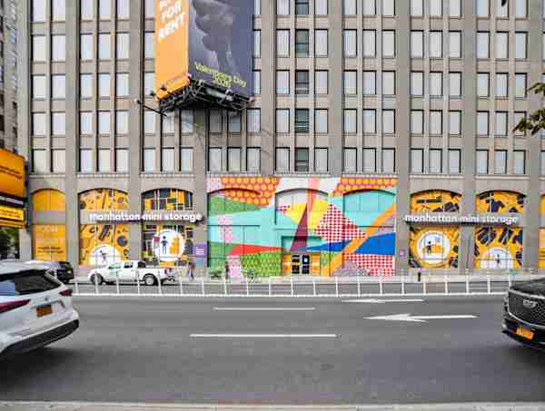 Manhattan Mini Storage building on 260 Sprint St with vibrant street art mural on facade and a yellow NYC taxi passing in the foreground.