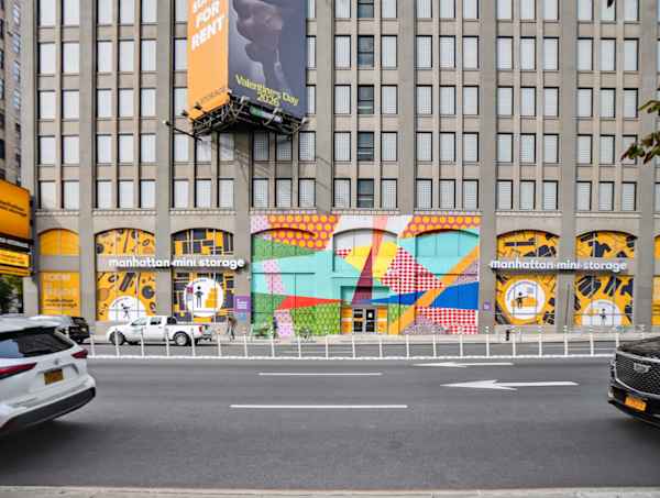 Manhattan Mini Storage building on 260 Sprint St with vibrant street art mural on facade and a yellow NYC taxi passing in the foreground.