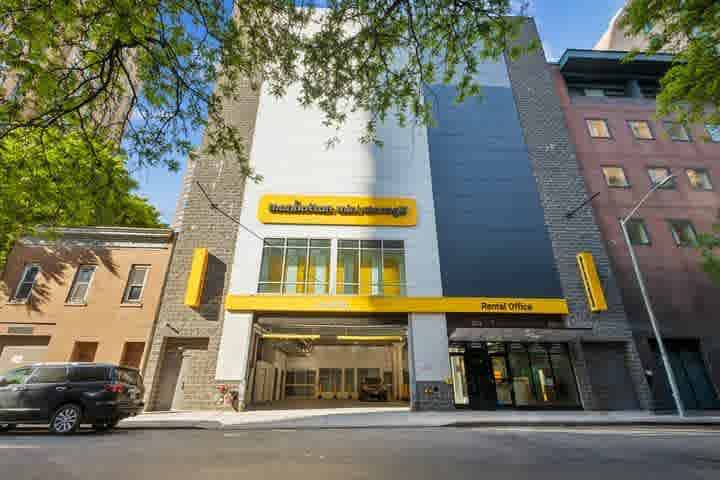 Street view of a modern Manhattan Mini Storage facility with a bright yellow awning labeled 'Loading' and 'Rental Office,' showing the open indoor loading bay and entrance on a sunny day.