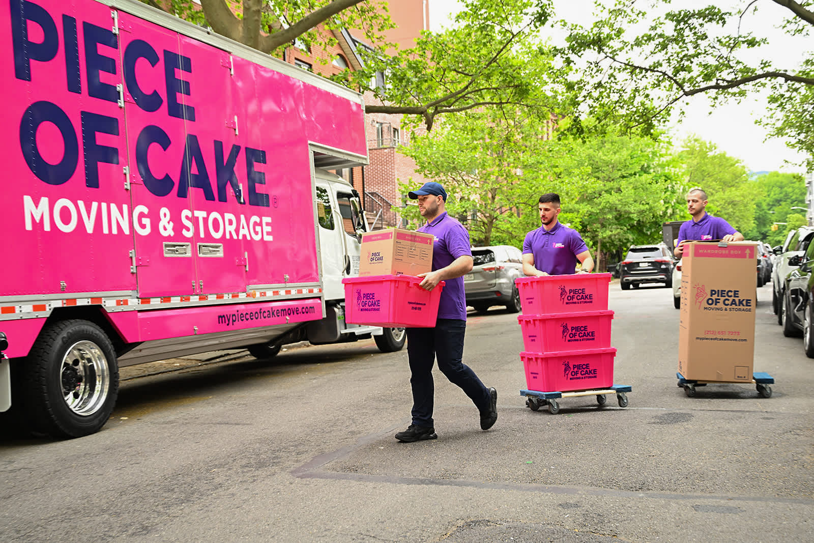 Piece of Cake movers carrying boxes to a pink Piece of Cake moving truck