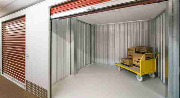 a large self storage unit with the door open and a moving cart in the corner stacked with moving boxes