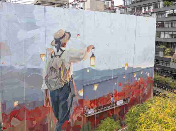 a mural painted on the side of the Manhattan Mini Storage building on W 21st Street shows a child with a backpack carrying a lantern