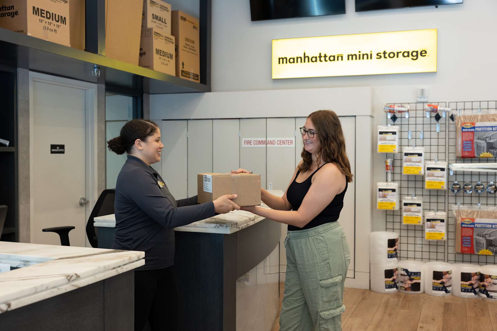 a smiling Manhattan Mini Storage employee hands a young woman a packing in the office