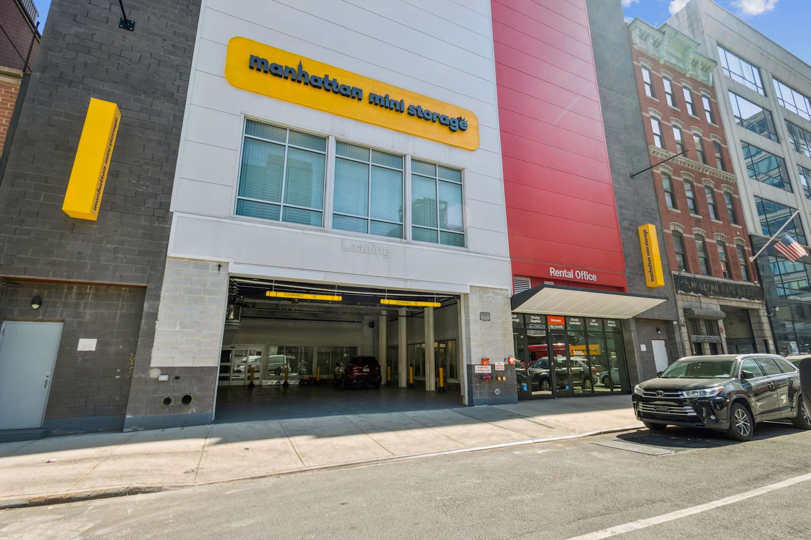 Manhattan Mini Storage - view from the street showing the brand logo, a large drive-in loading bay, and the front office door