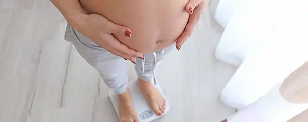 Pregnant woman standing on scales to track her weight gain