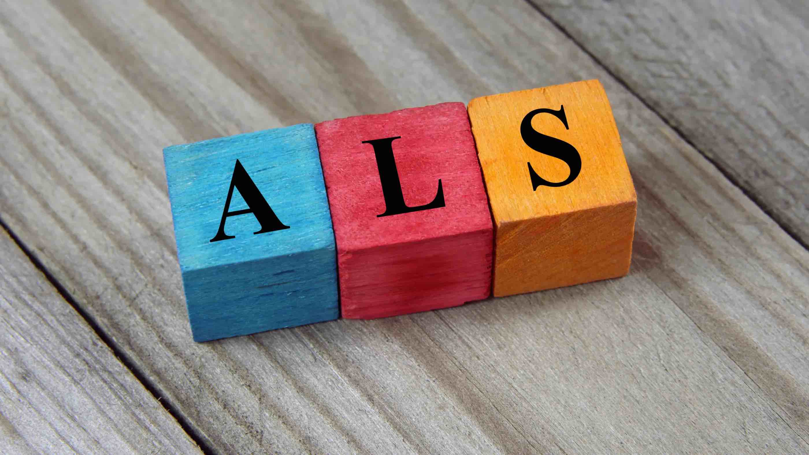 Wooden blocks spelling ALS on a wooden surface