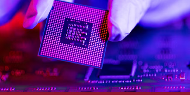 The engineer's gloved hand is holding the CPU chip against the background of the motherboard.