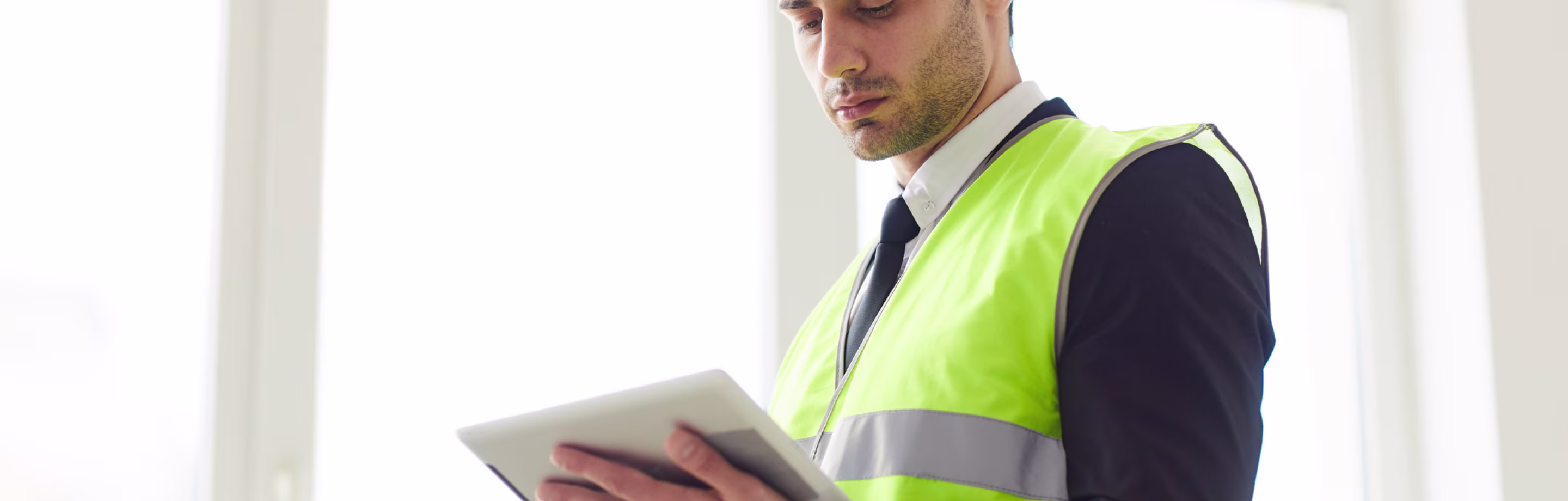 Waist-up portrait of Middle Eastern engineer wearing hardhat standing against window holding tablet
